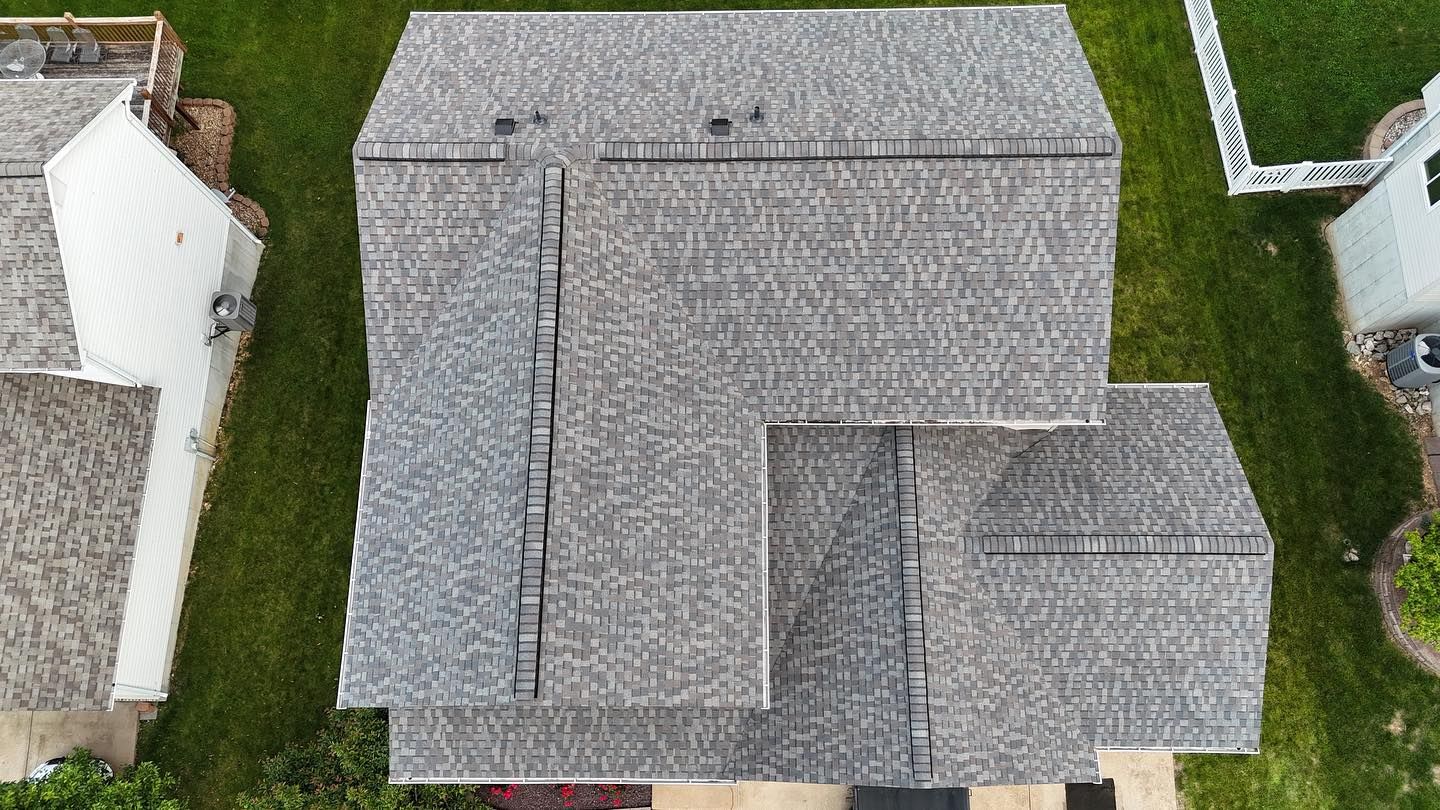 Overhead view of a house with gray shingle roof, surrounded by green grass and a neighboring white house.