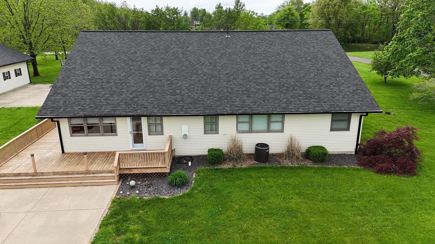 Low-angle view of a beige house with black roof, wooden deck, and green lawn.