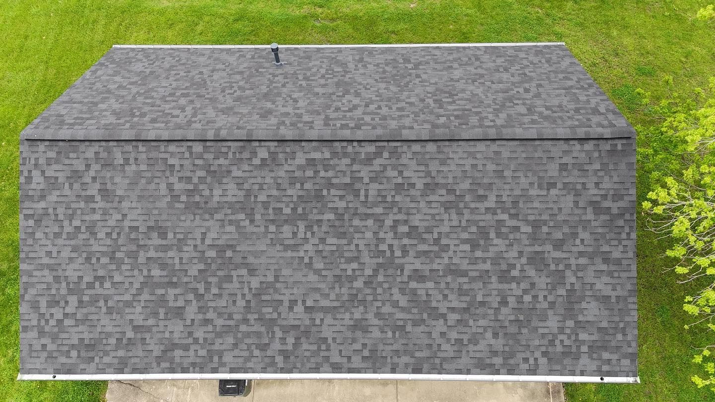 Overhead view of a gray asphalt shingle roof on a building, set against green grass.