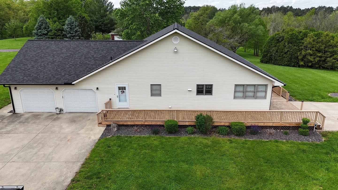 Beige ranch-style house with attached garage, wooden deck, and green lawn. Driveway in front.