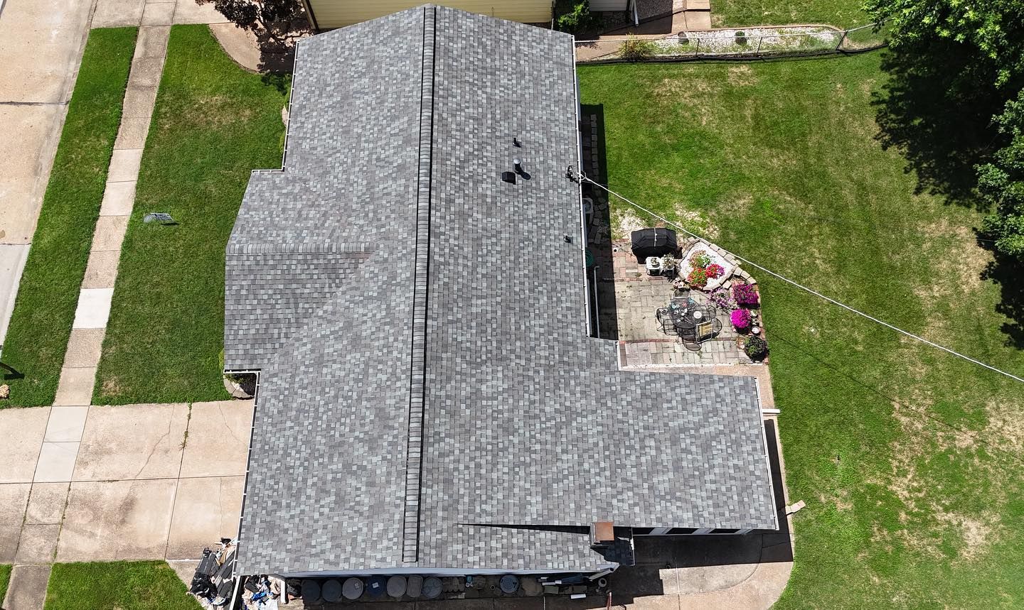 Overhead view of a house with a gray shingle roof, surrounded by green grass and a concrete driveway.