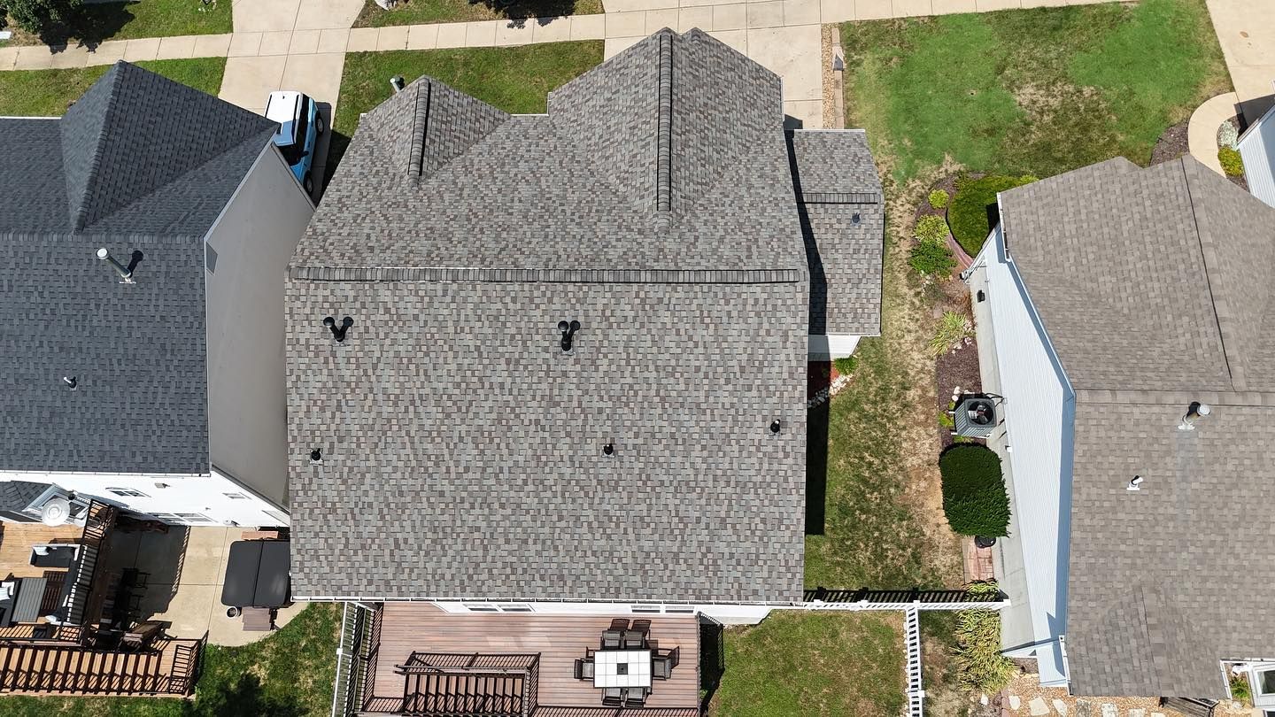 Aerial view of a gray roofed house, next to other houses with green lawns.
