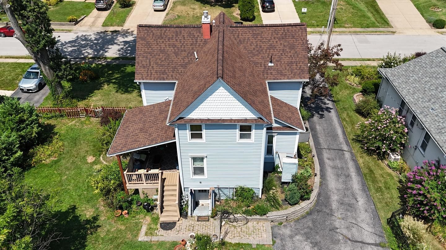 Aerial view of a light blue two-story house with a brown roof and a porch.