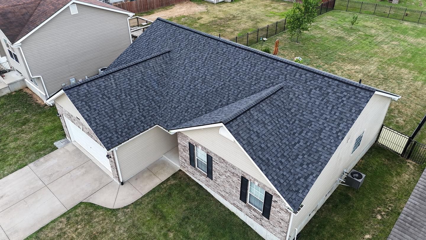 Overhead view of a house with a dark gray shingled roof, beige siding, and a concrete driveway.