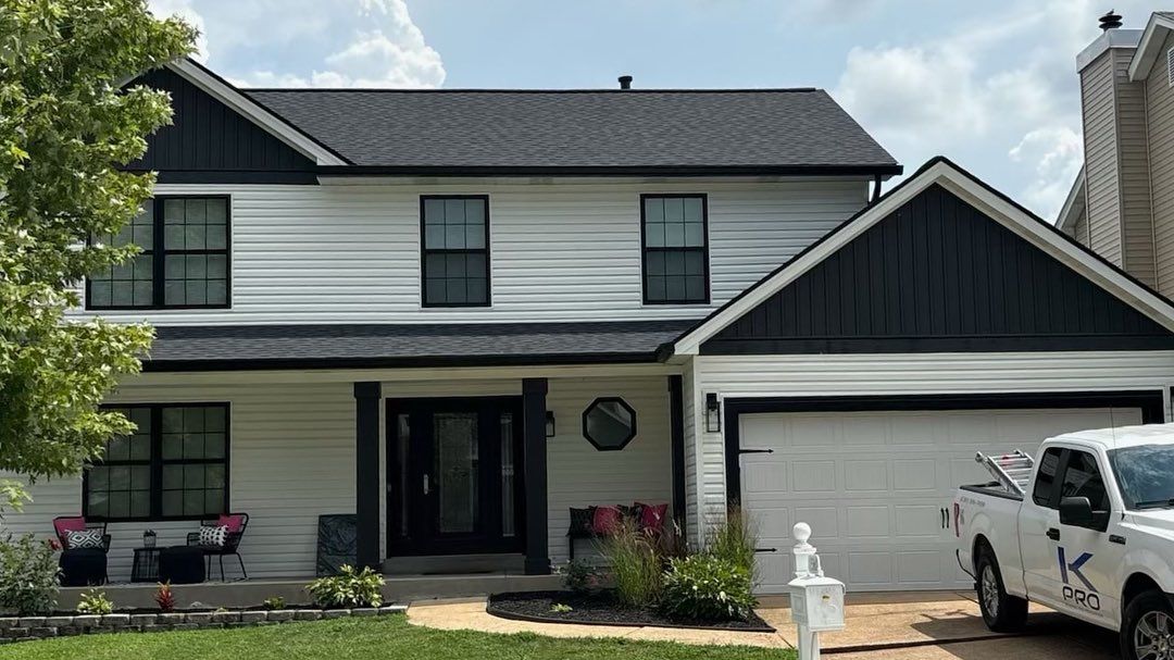 White house with black trim, black roof, and white garage door. A white truck is parked nearby.