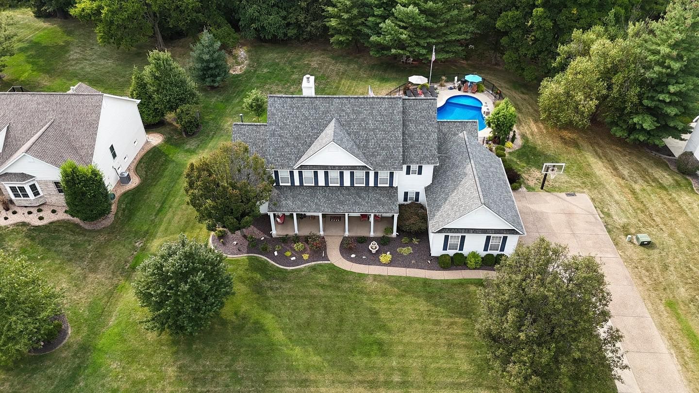 Aerial view of a white two-story house with a grey roof and a swimming pool in the backyard.
