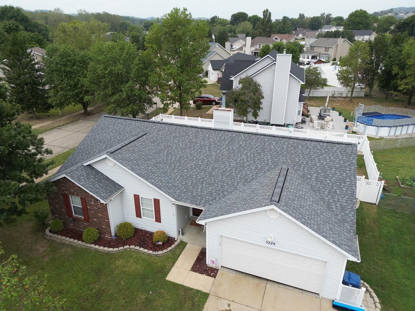 A suburban home with a gray roof, white siding, and a red front door, surrounded by trees and a green lawn.