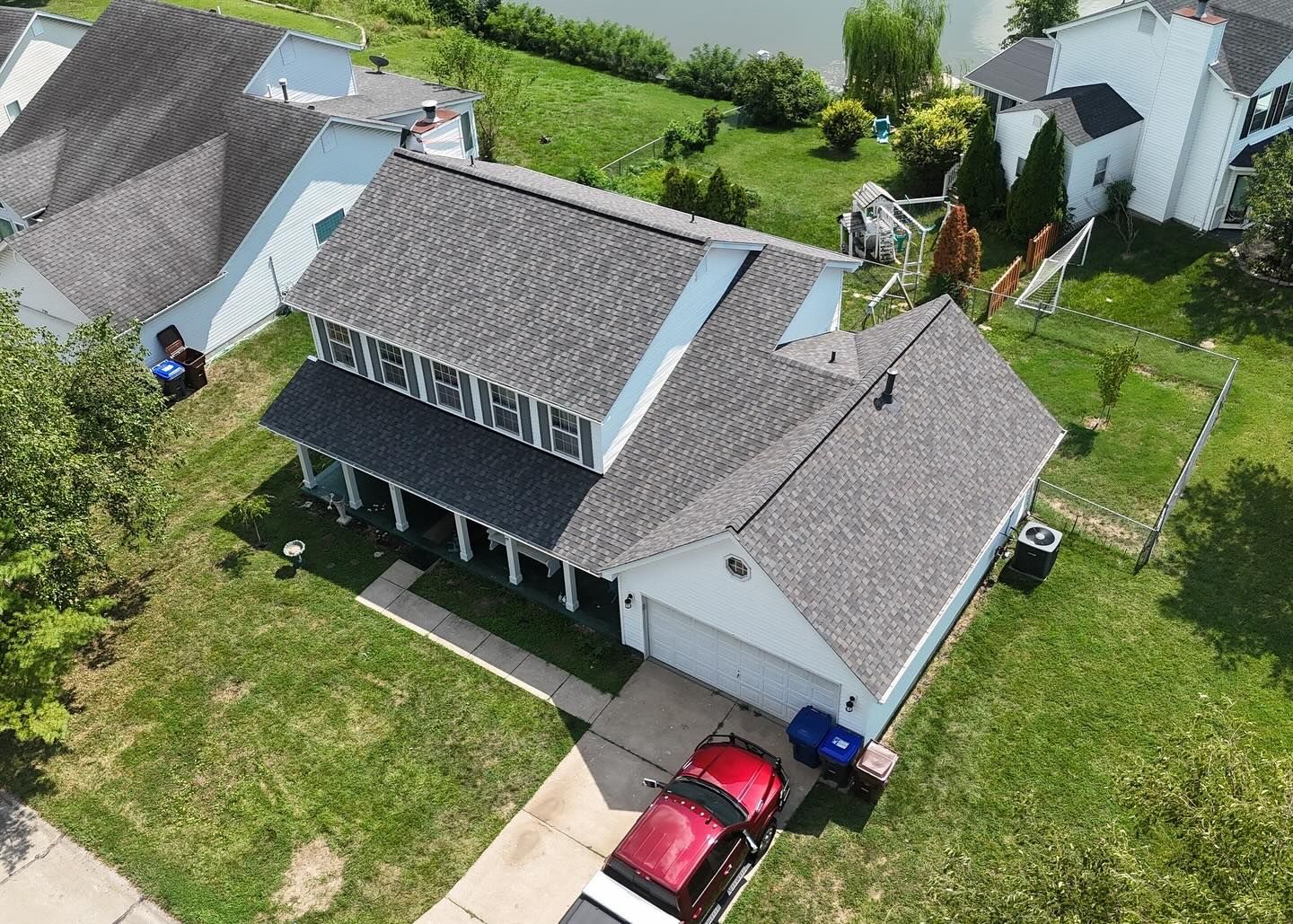 Aerial view of a white two-story house with a gray roof, a driveway, and a red car.