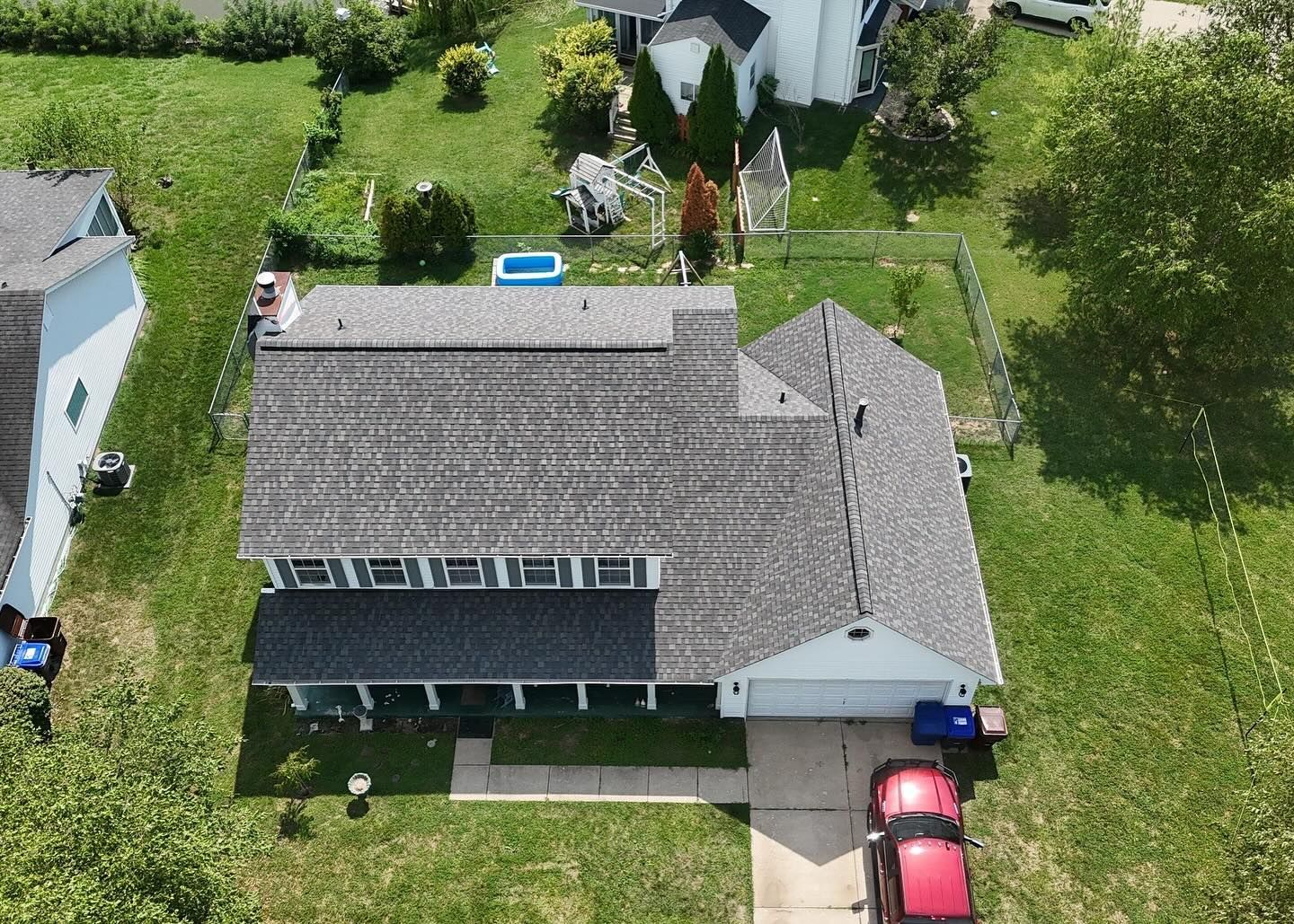 Aerial view of a two-story house with a grey roof, green lawn, and red car parked in the driveway.