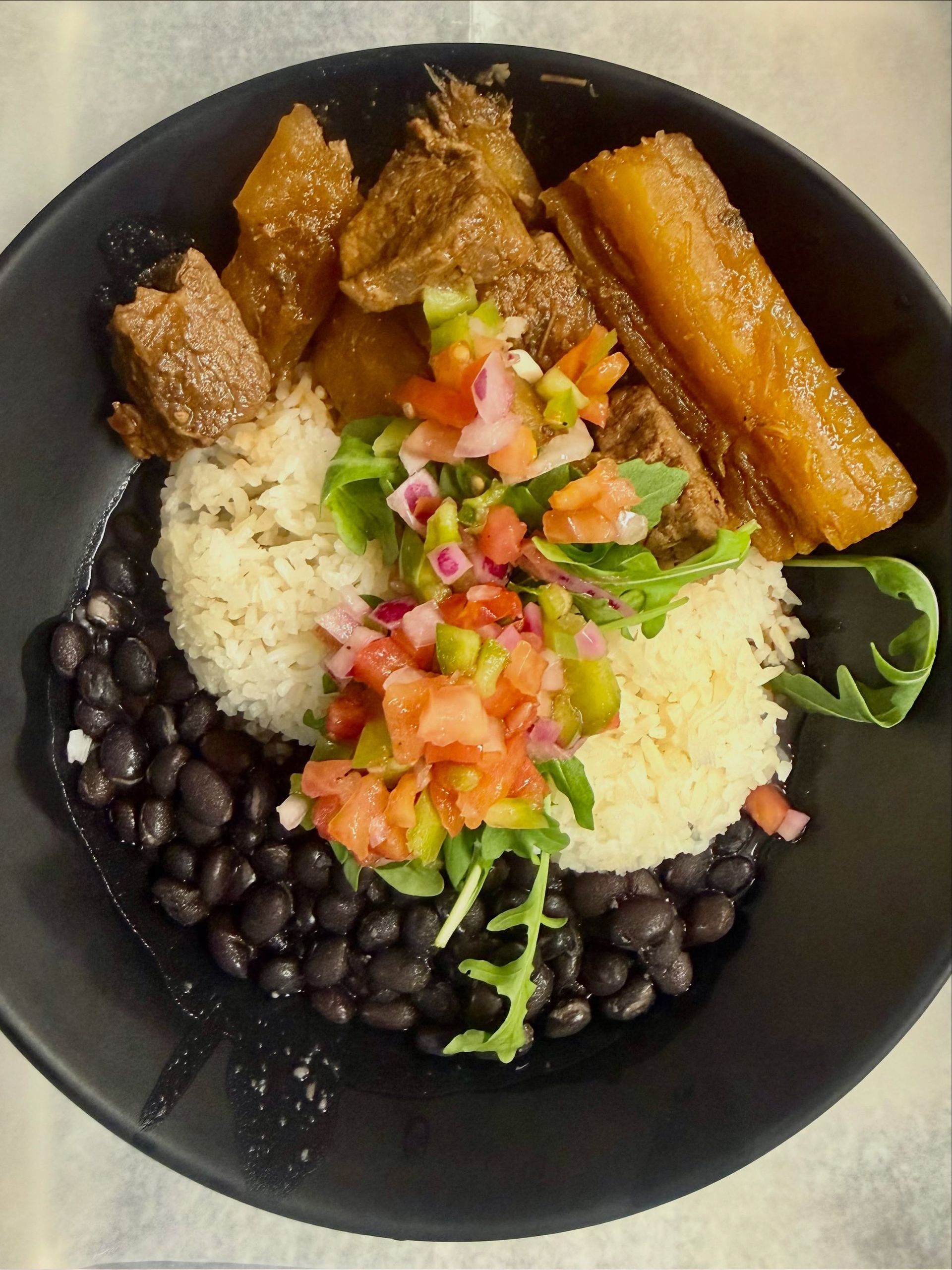 Rice bowl with black beans, plantains, and diced tomato-cilantro salsa in a black bowl