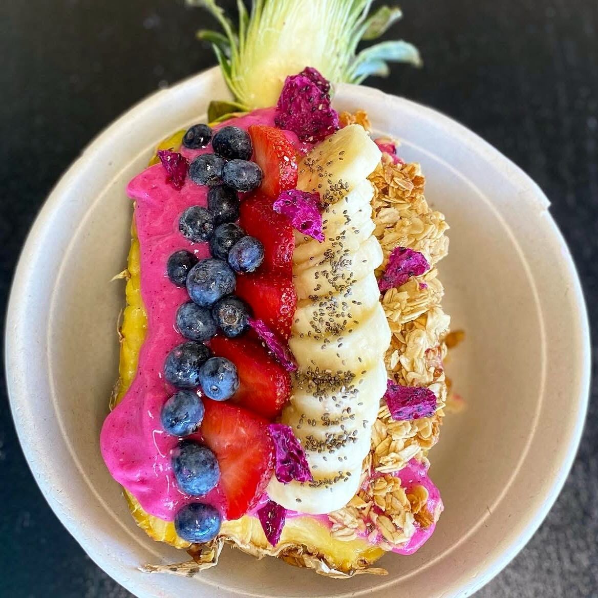 Pineapple bowl filled with pink smoothie, blueberries, strawberries, banana, dragon fruit, and granola.