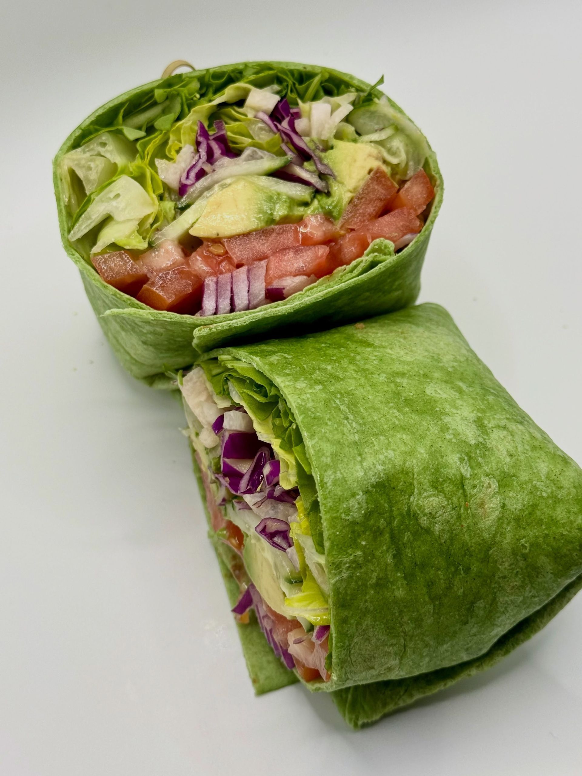 Two green wraps stuffed with lettuce, tomato, and red cabbage, one standing upright and one folded over.