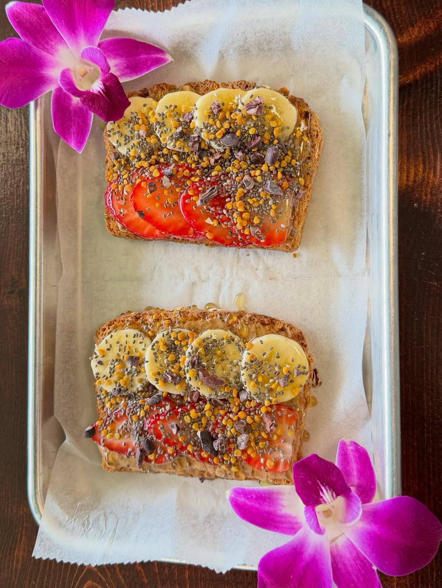 Two fruit and granola toast slices on a tray, garnished with purple orchids.