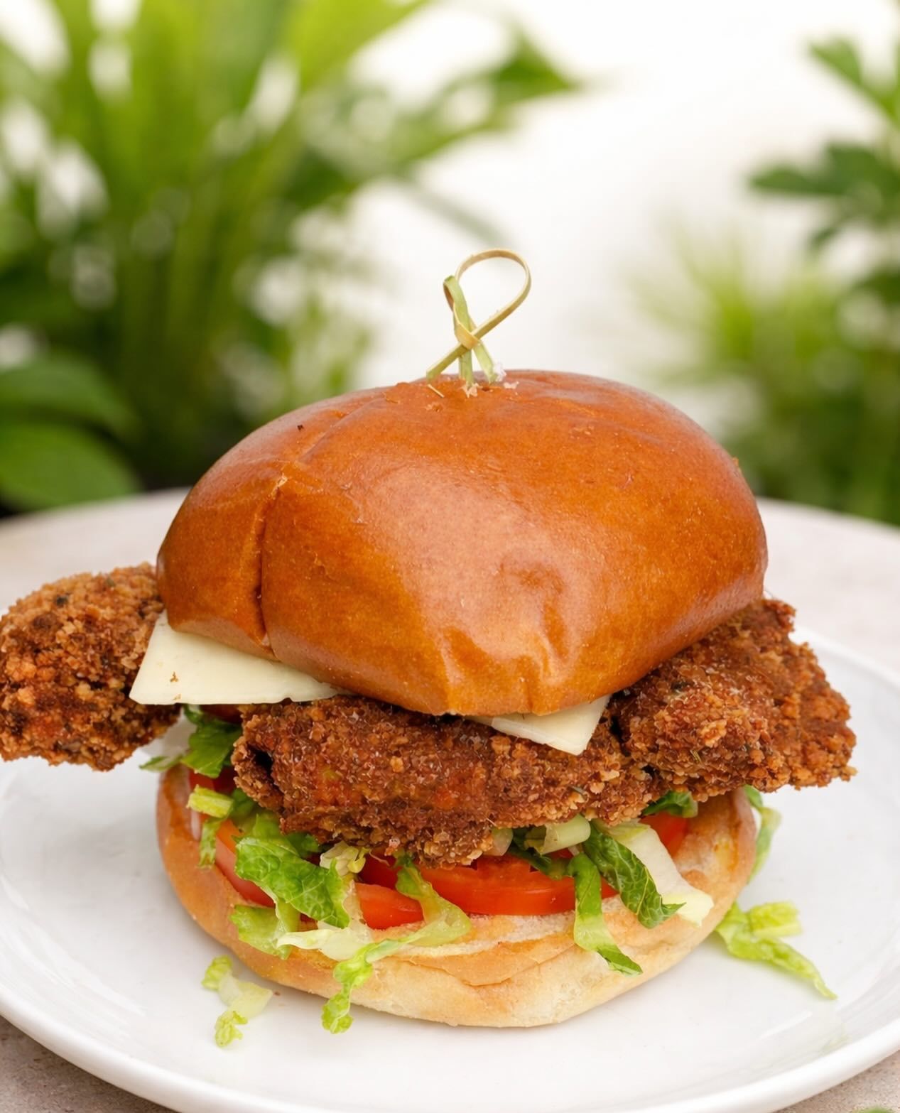 Fried chicken sandwich with lettuce and tomato on a white plate, topped with a glossy brioche bun