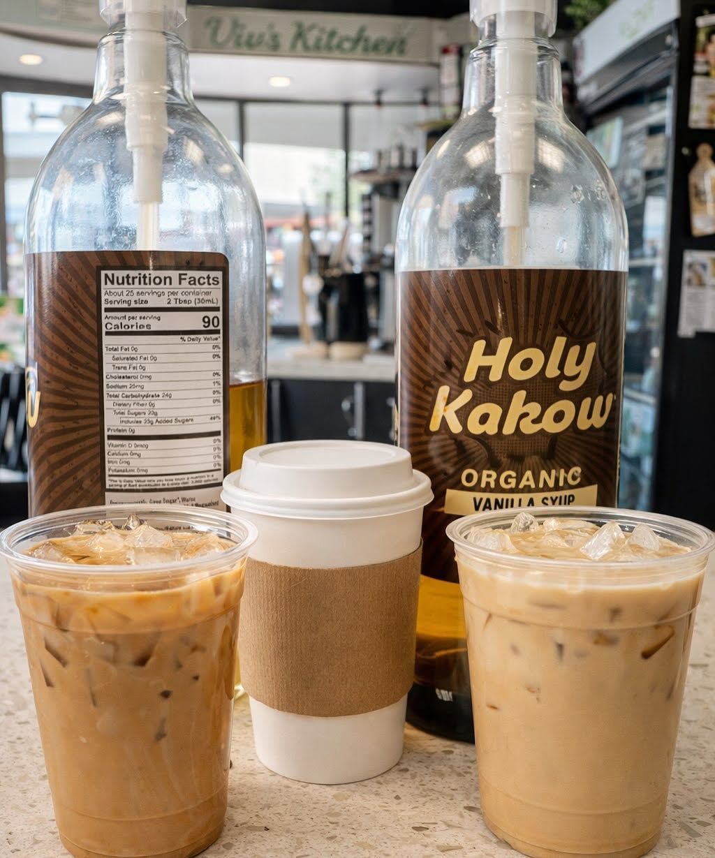 Two iced coffees and a hot coffee in a café, with two Holy Kakow syrup bottles behind them.
