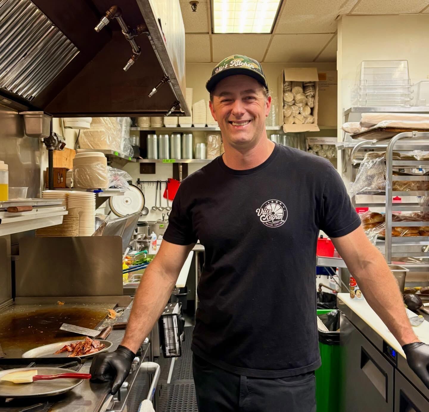 Smiling chef in a black shirt standing in a busy restaurant kitchen
