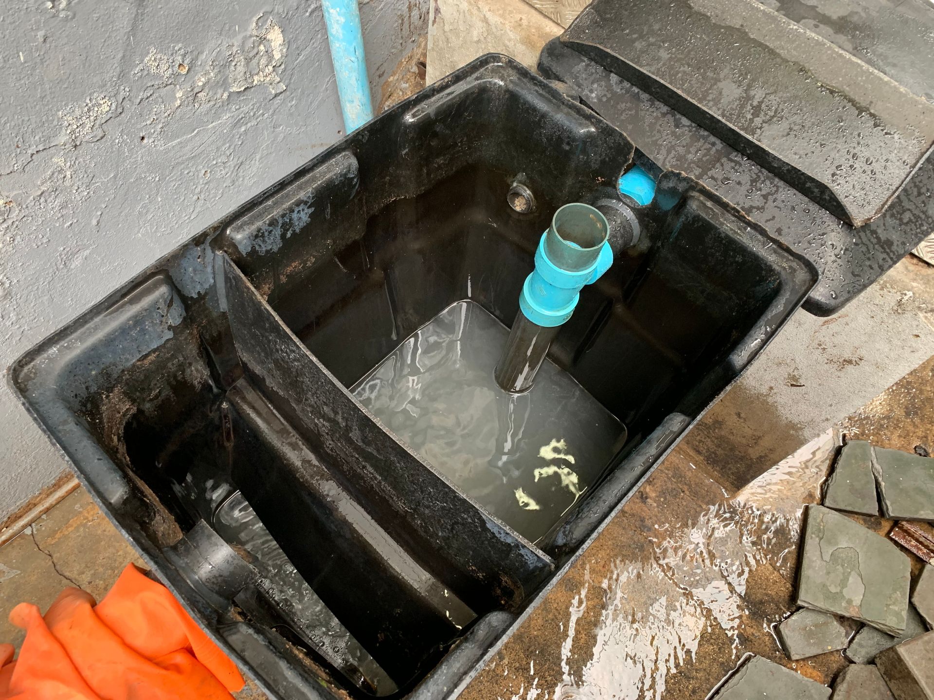 Black rectangular water filtration box with water and blue pipe, outside.