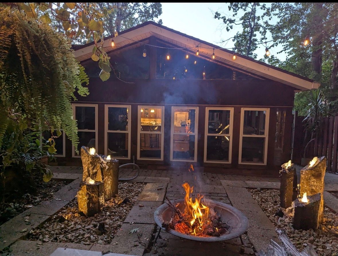 Cozy cabin patio at dusk with string lights, fire pit, and candles glowing in the yard
