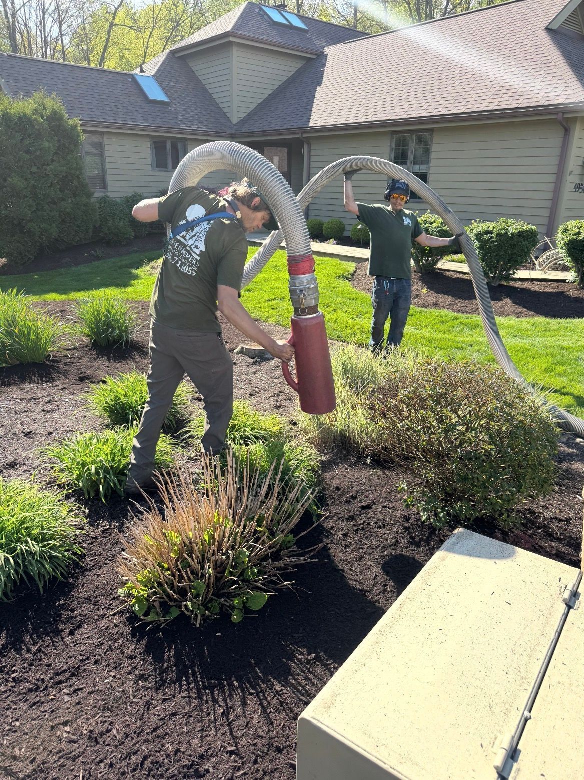 Two workers using a hose to clean a landscaped yard beside a house