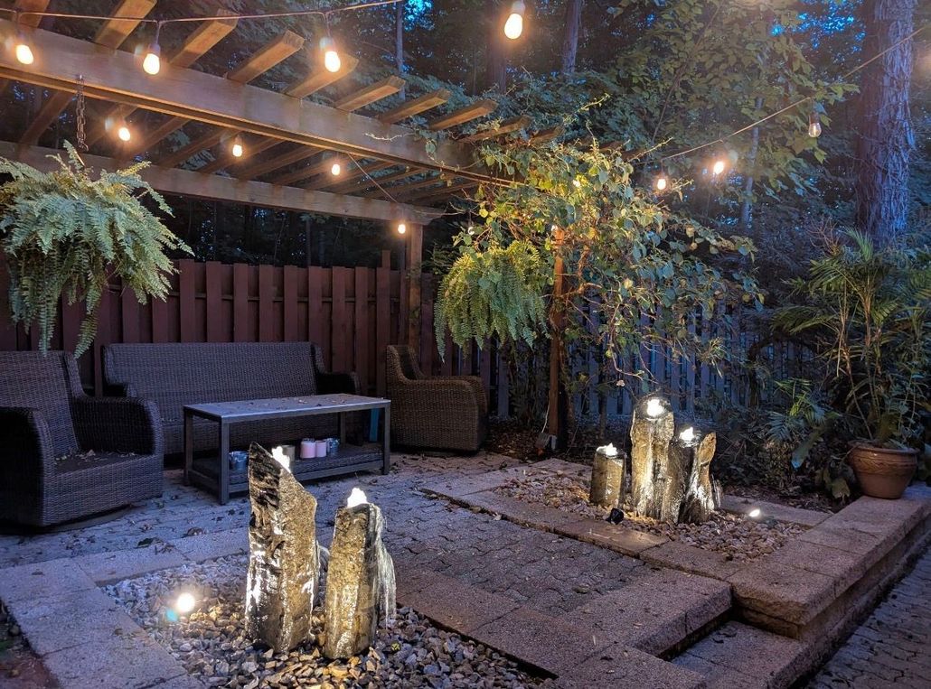 Cozy outdoor patio with string lights, wicker seating, and glowing lanterns among greenery and gravel paths