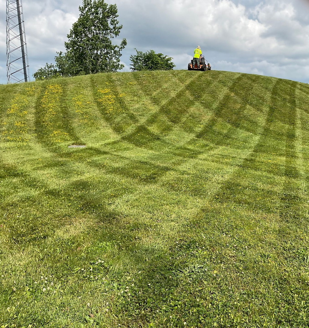 Freshly mowed grassy hill with diagonal tire tracks and a worker in a yellow vest at the top