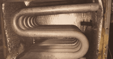 Serpentine metal tubes inside a rectangular enclosure, likely a furnace component.