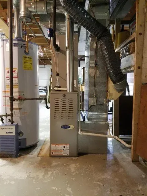 A furnace and water heater in a basement. Ductwork and plumbing are visible. The floor is concrete.