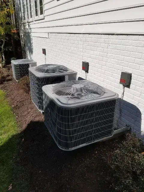 Three air conditioning units aligned against a white brick wall, with small control boxes.