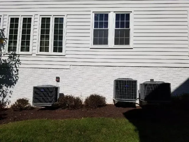 Three air conditioning units sit below windows of a white house.