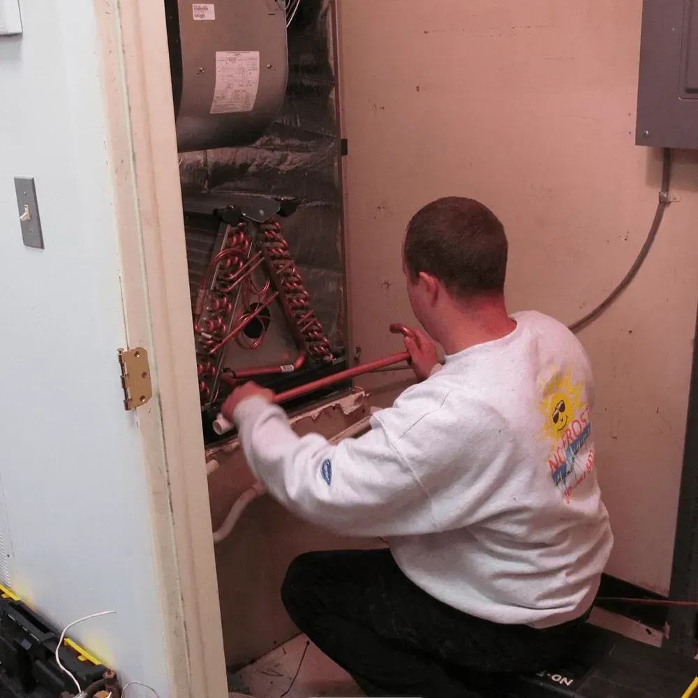 Man working on HVAC system in a utility closet. He is using tools to adjust copper pipes.