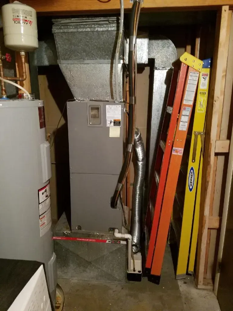 Furnace and water heater in a utility room with two ladders leaning against the wall.