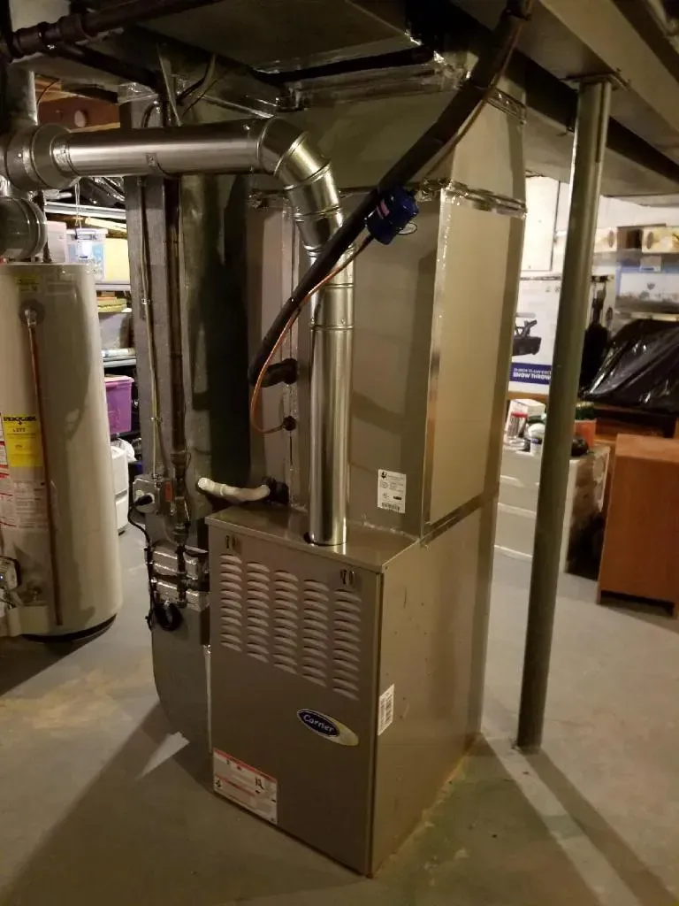 Furnace and ductwork in a basement. Beige furnace with metal ducting, connected to pipes.