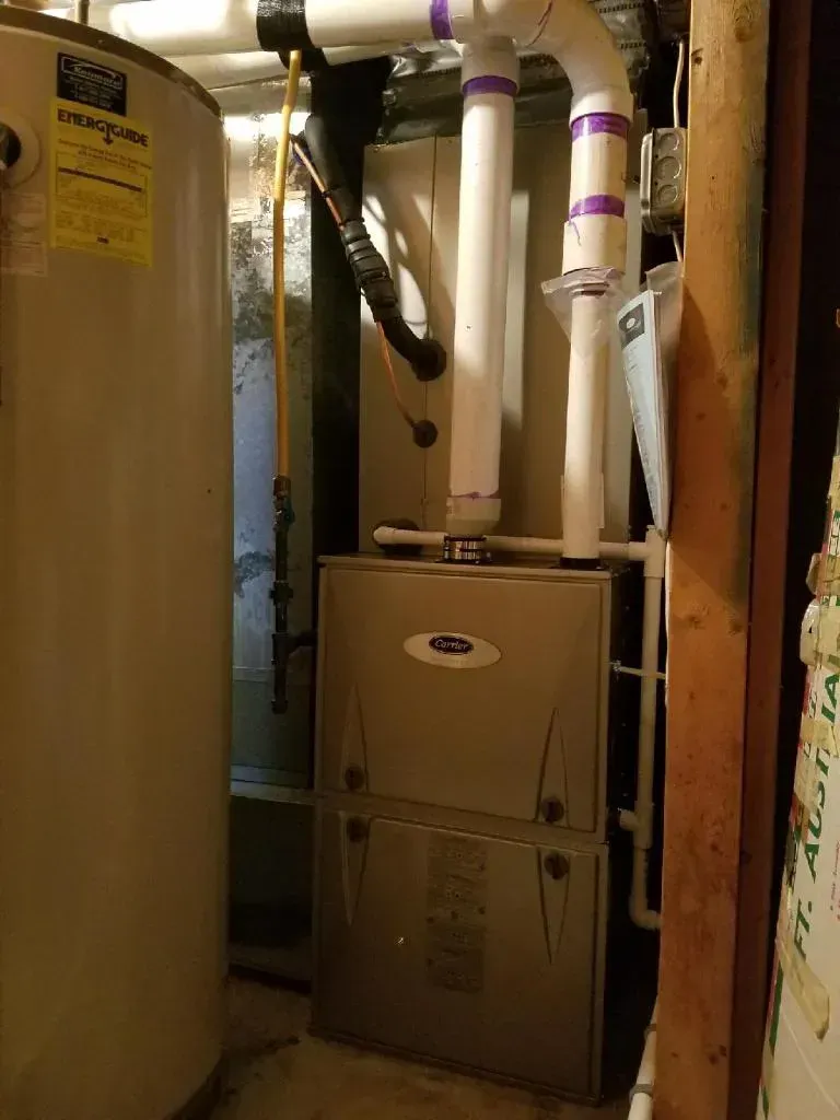 Furnace and water heater in a basement. White pipes, a yellow gas line, and a gray metal furnace.