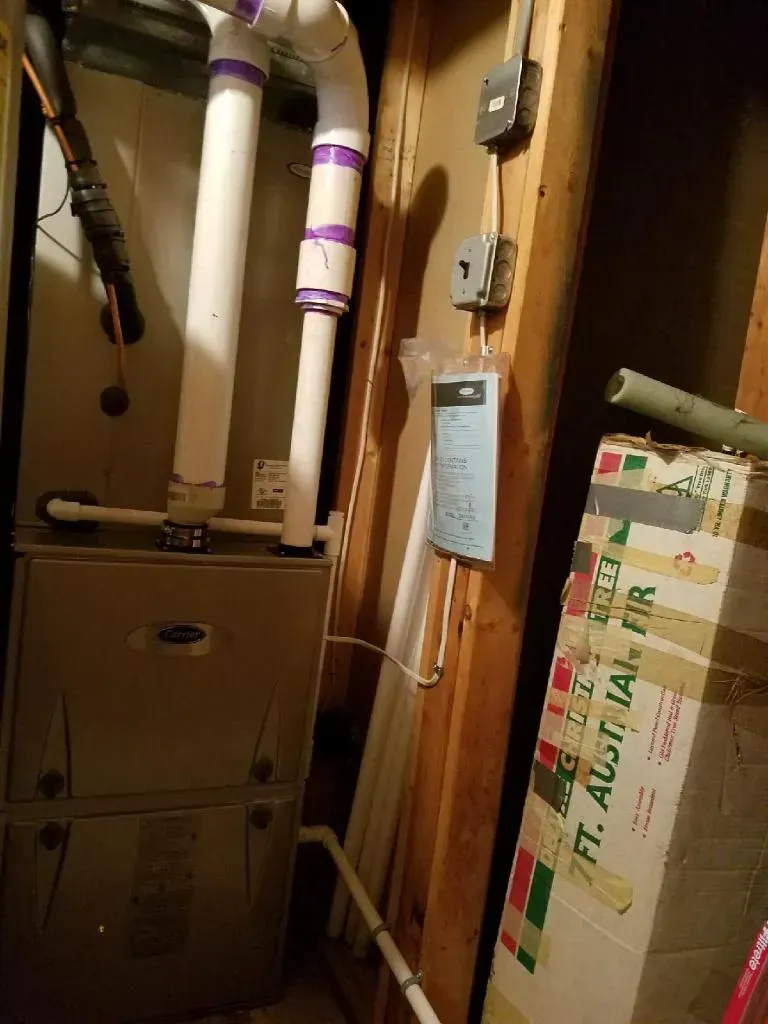 Furnace in a basement; white PVC pipes, electrical box, and a cardboard box.