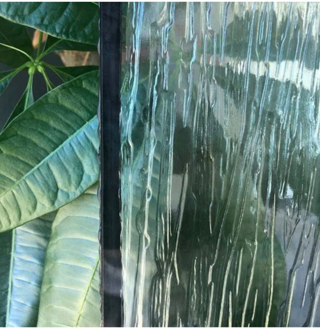 Green leaves next to textured glass with vertical streaks; black border.