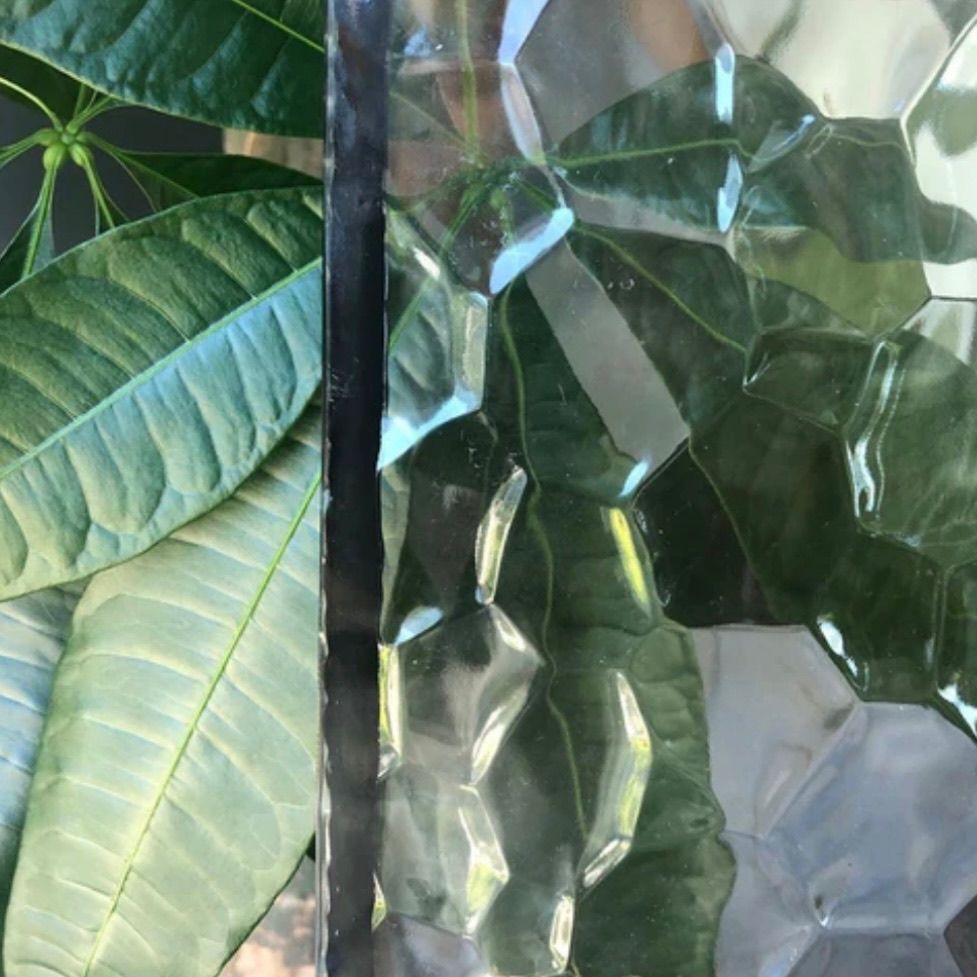 Green leaves beside textured glass with light reflections.