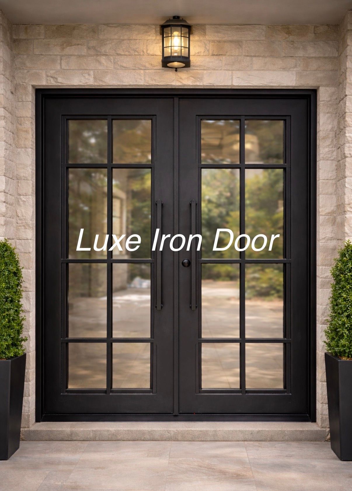 A black, double-paneled iron front door with glass grid windows, flanked by two topiaries against a stone wall.