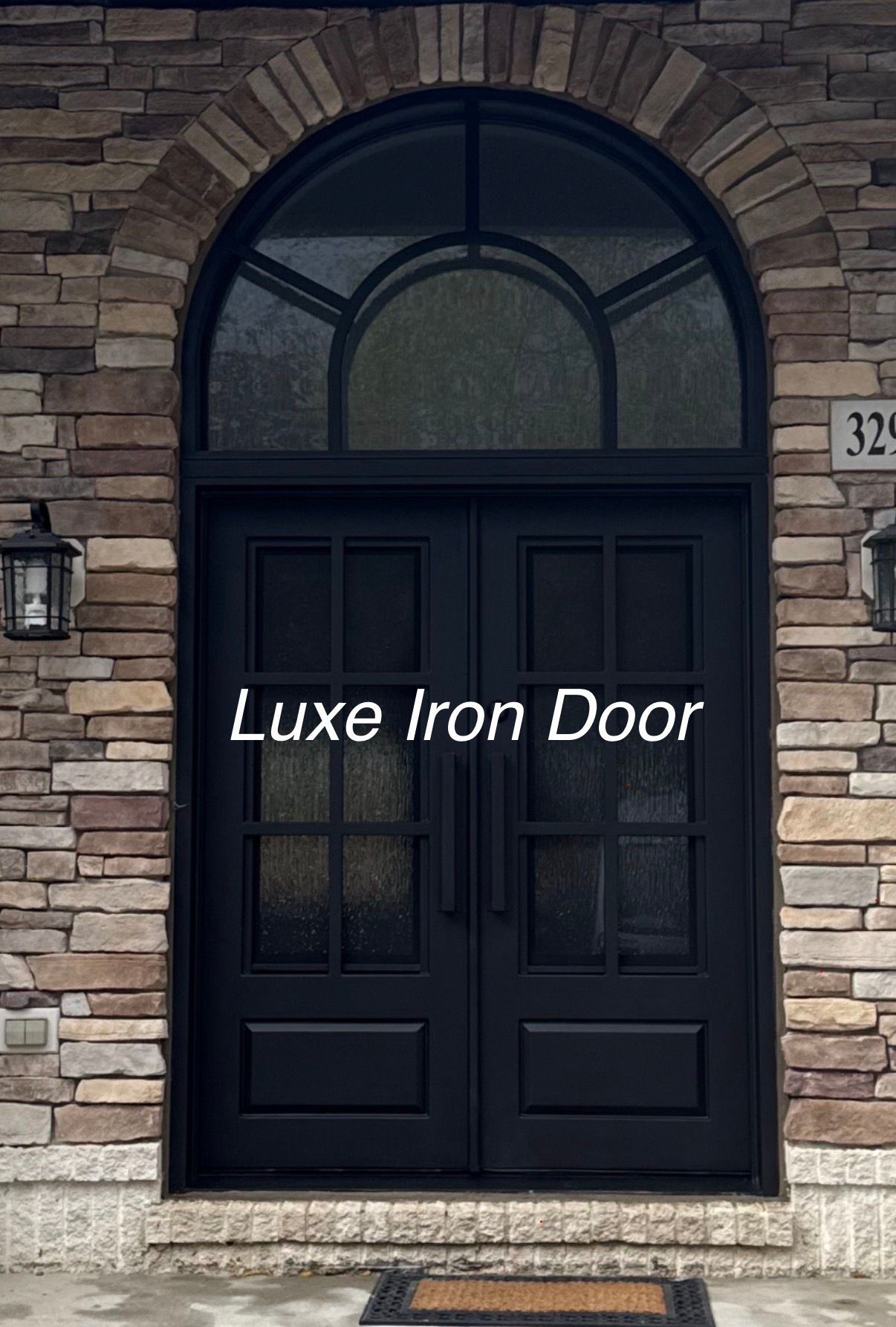 Black double iron front doors with glass panes and an arched transom window set into a stone exterior wall.