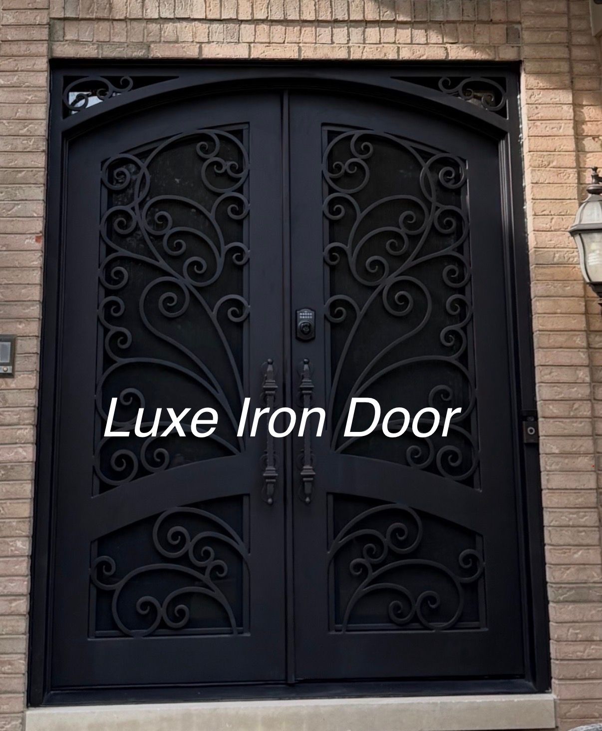 A black, double-entry iron door with intricate scrollwork, set within a light-colored brick wall.