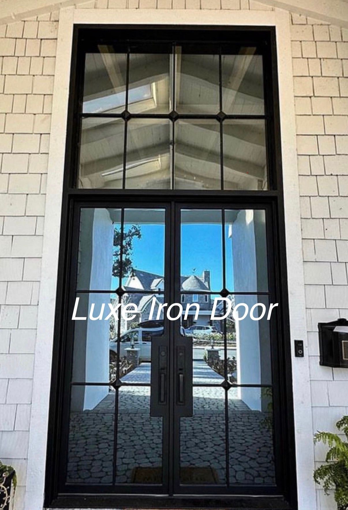 Black double iron doors with a glass transom, set into a white shingled exterior wall.