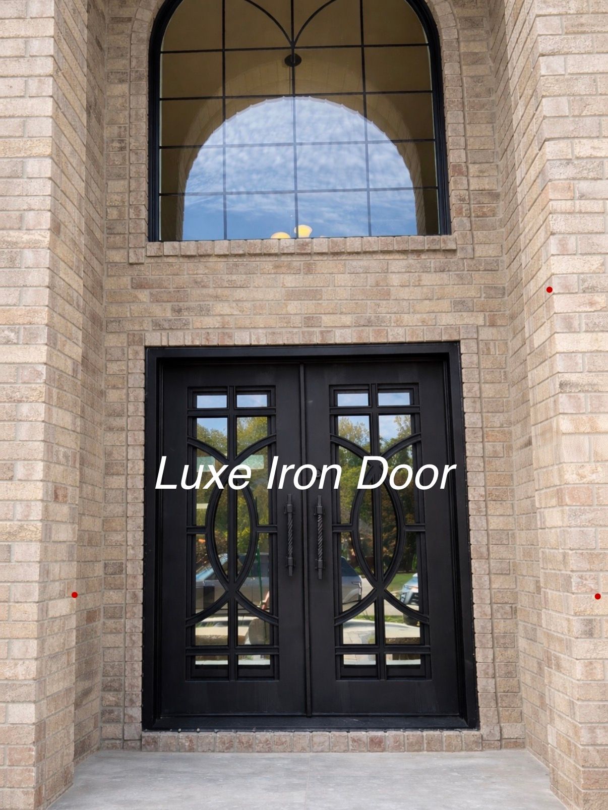 Black iron double front door beneath an arched window in a stone entryway