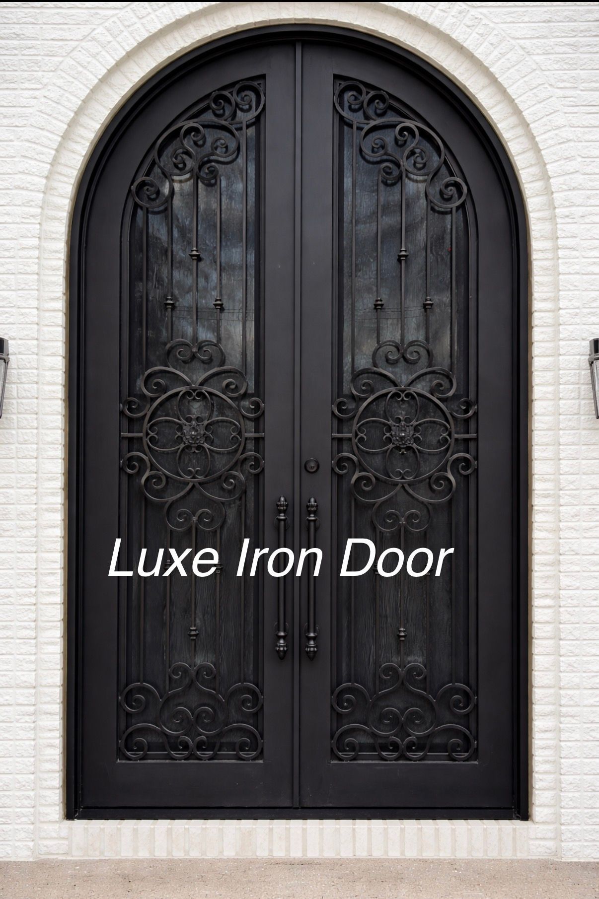 Black arched iron double front door with ornate scrollwork in a white brick wall
