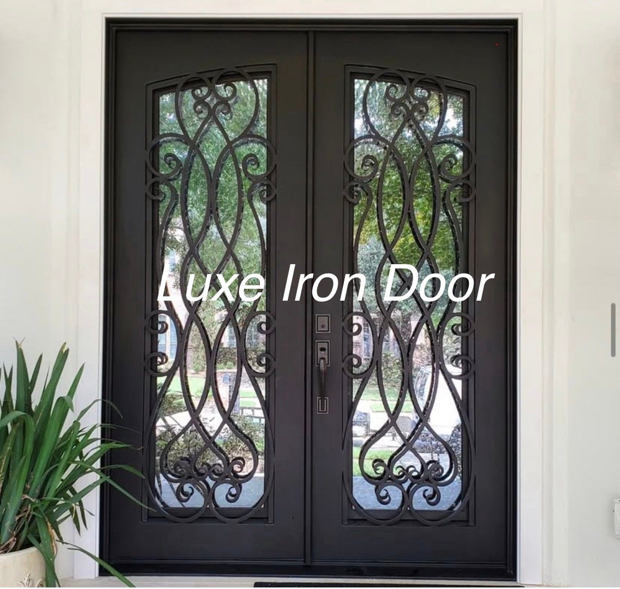 Black double iron front door with ornate glass panels and a plant beside it