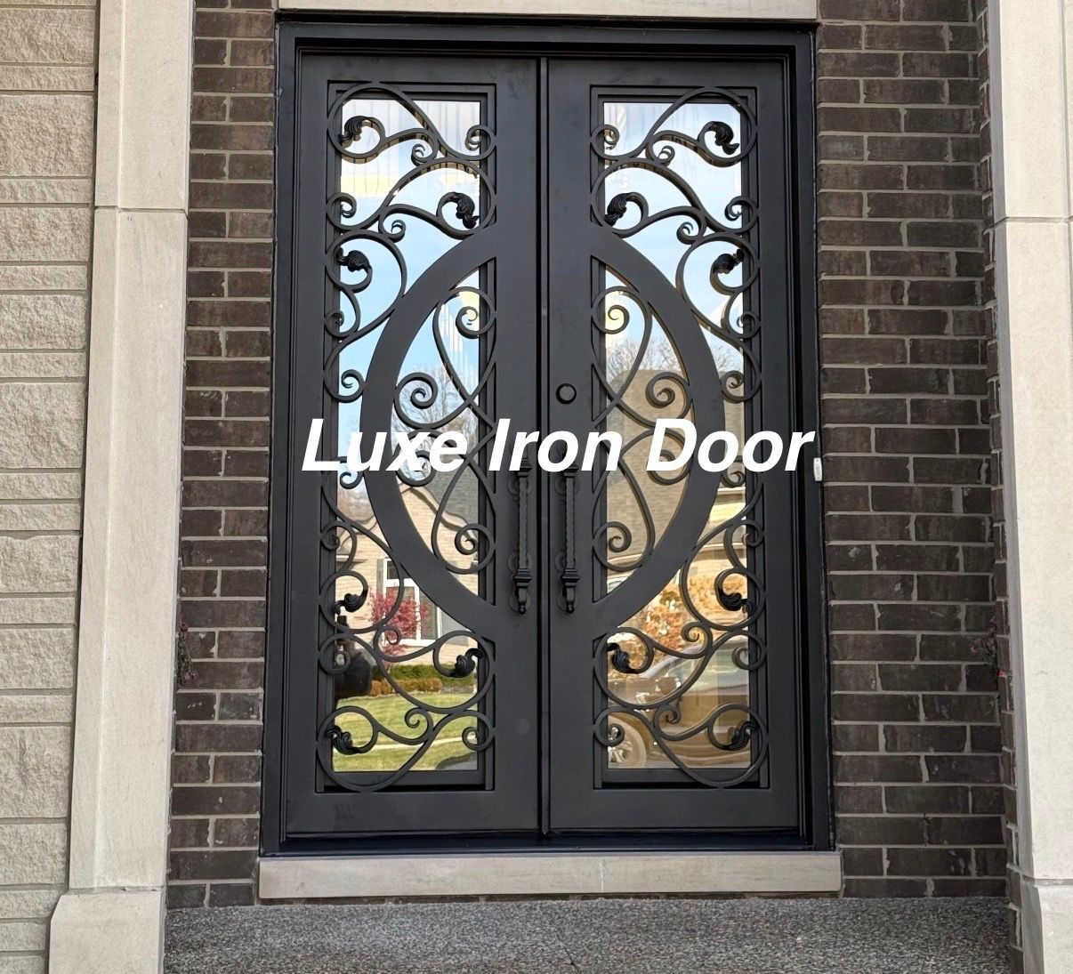 Black iron double front door with ornate glass panels in a brick entryway