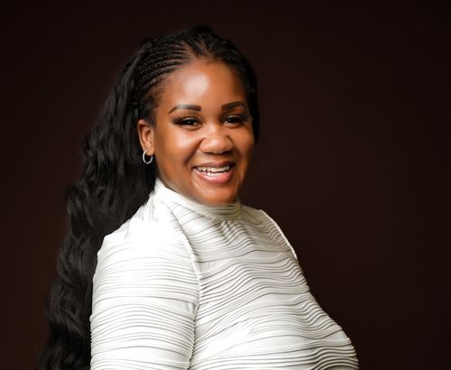 Smiling person in a white textured top against a dark brown background.