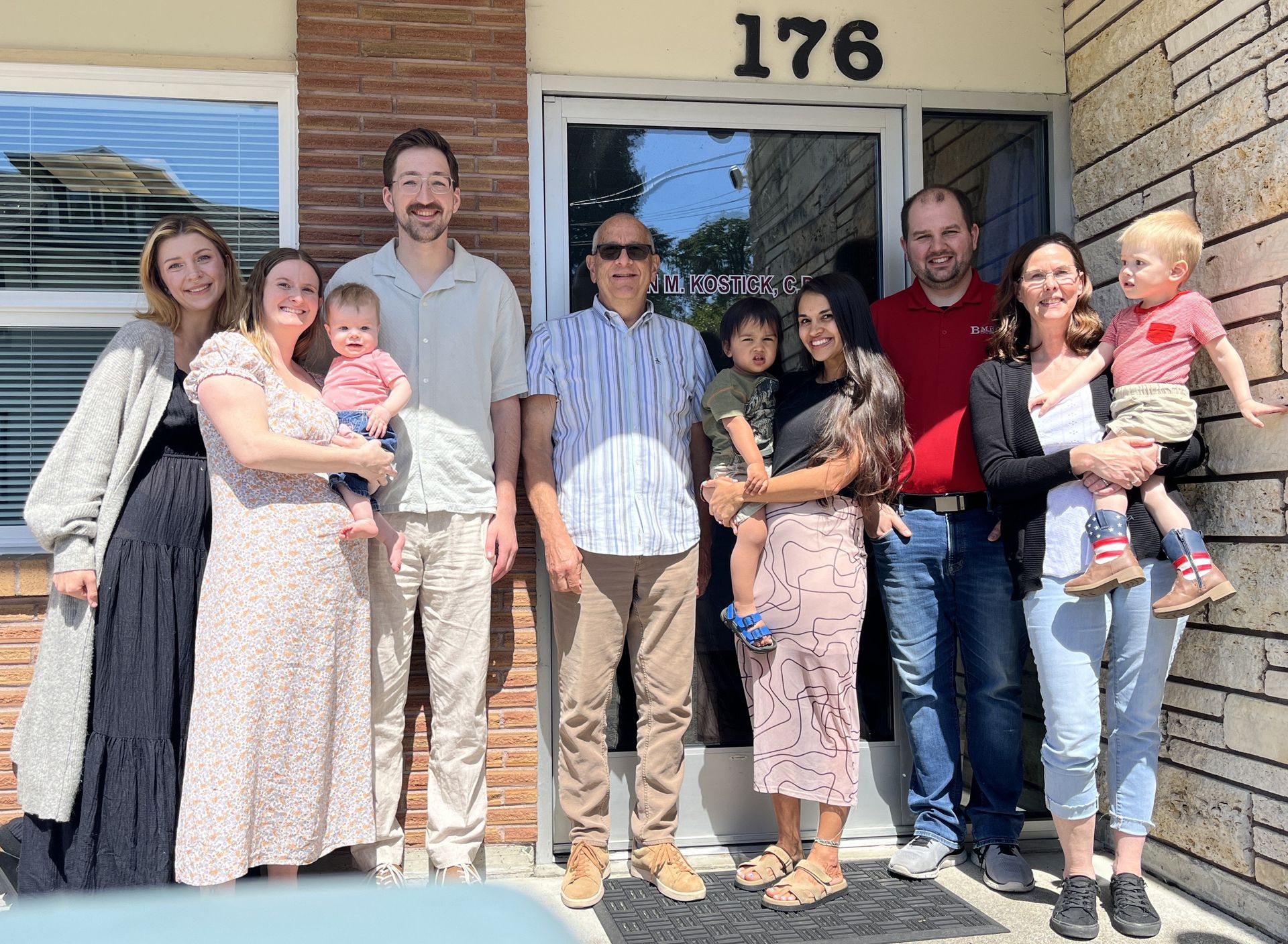 Group of adults and children smiling outside a building with the number 176 on the door.