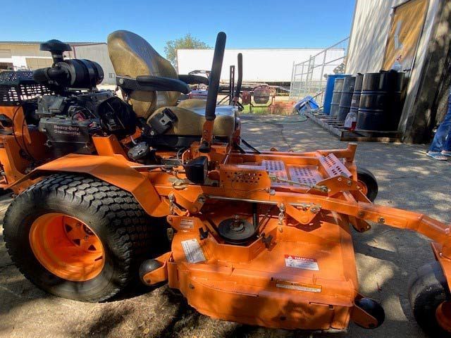 An orange lawn mower is parked in front of a building.