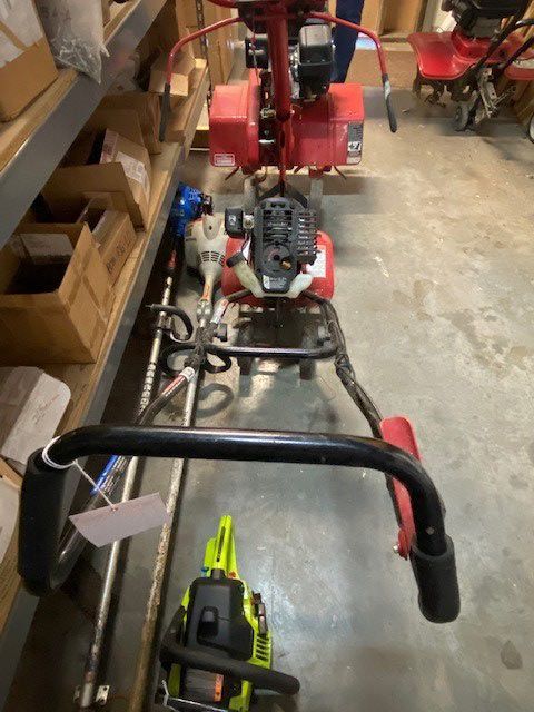 A red lawn mower is sitting in a warehouse next to a chainsaw.