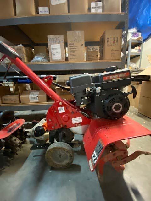 A red and black lawn mower is sitting in a warehouse.