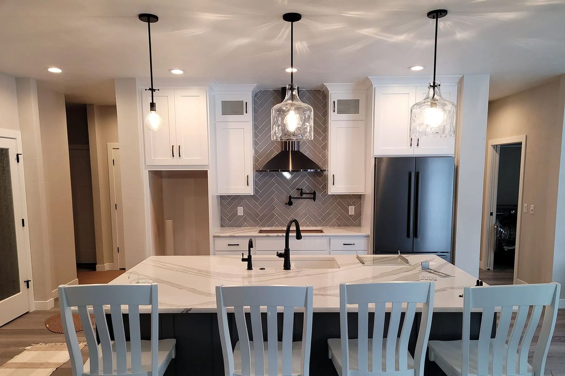a kitchen with white cabinets, a large island, a refrigerator and a sink